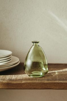 a green glass vase sitting on top of a wooden shelf next to plates and bowls