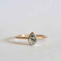 a yellow gold ring with a green stone in the center on a white table top