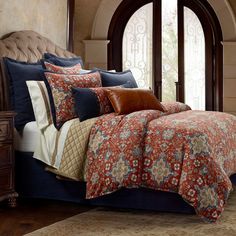 a bed with red and blue comforters in a bedroom next to an arched window