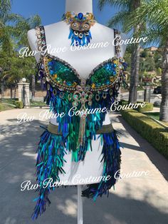 a mannequin with blue and green feathers on it's chest, in front of palm trees