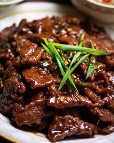 a white plate topped with meat covered in sauce and garnished with green onions