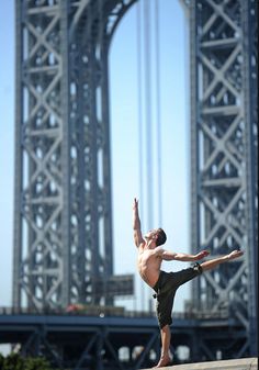 a man standing on one leg in front of a bridge