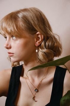 a woman with blonde hair wearing a black top and gold necklace, looking off to the side