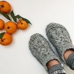 a person's feet in knitted slippers next to oranges on a white surface