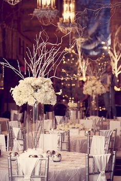 the centerpieces are decorated with white flowers and branches in silver vases on tables