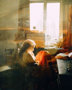 a woman sitting at a desk in front of a window with sunlight streaming through it