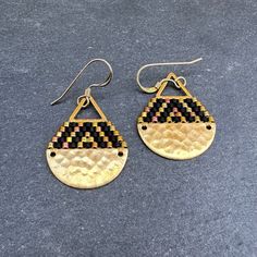 These brick stitch and brass beaded earrings were handwoven with Miyuki glass seed beads. A time intensive and intricate craft, each bead is carefully hand stitched in order to create an even, uniform weave. The process requires focus, patience and dedication, as even a small pair of earrings can take hours to complete. The tiny glass seed beads are incredibly lightweight, so even the larger size statement earrings can be comfortably worn all day long.  Handwoven Brick Stitch Beadwork Miyuki glass seed beads (Glass and 24k gold plated)  14k gold filled ear wires  Hammered raw brass half moon piece Brass triangle component Extra durable nylon beading thread Each bead is approx. 1.6mm x 1.3mm Size: 1 1/4" long (including ear wire), 3/4" wide Weight: 1g each (2g/pair) Gold Woven Round Beads Jewelry, Handwoven Teardrop Jewelry As Gift, Artisan Brass Jewelry With Tiny Beads, Bohemian Handwoven Brass Earrings, Gold Fair Trade Beaded Jewelry, Handwoven Gold Drop Earrings, Handwoven Brass Beaded Dangle Earrings, Gold Handwoven Drop Earrings, Adjustable Handwoven Teardrop Jewelry