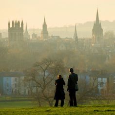 two people standing on top of a lush green field next to a tall city skyline