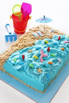 a cake with blue frosting and beach scene on the top is sitting on a table