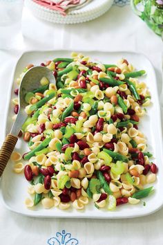 pasta salad with beans and green beans on a white platter next to silverware