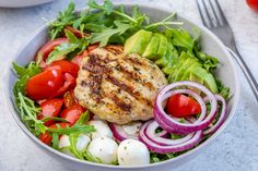 a white bowl filled with salad and meat topped with tomatoes, onions, cucumbers, lettuce