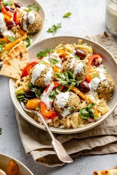 two plates of pasta with meatballs and veggies next to pita bread