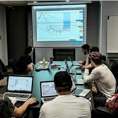 a group of people sitting around a conference table with laptops and monitors on it