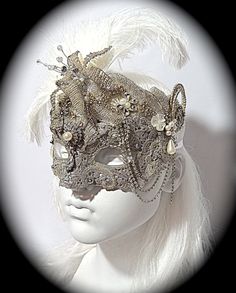 This opulent masquerade mask is platinum silver with lace overlays and gorgeous vintage rhinestone appliques that surround the top and cheeks. A vintage jewelry piece and a silver beaded flower are center on the forehead. The molded mask is loaded with rhinestones, gems, and vintage bead accents. Pearl drops & loops of rhinestone chain add elegant touches to this Art Deco style mask. Sprays of white ostrich feathers frame the top and one ear. It ties with white satin ribbons in back and is f Elegant Silver Evening Masks, Glamorous Masquerade Mask For Carnival, Silver Fantasy Masquerade Mask For Carnival, Fantasy Silver Masquerade Mask For Carnival, Elegant Eye Mask For Masquerade, Vintage Masquerade Mask For Carnival, Fantasy Masquerade Mask For Wedding And Mardi Gras, Silver Fantasy Masks And Prosthetics For Party, Silver Fantasy Carnival Mask