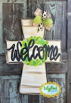 a welcome sign hanging on the side of a wooden door with a green wreath and polka dot bow