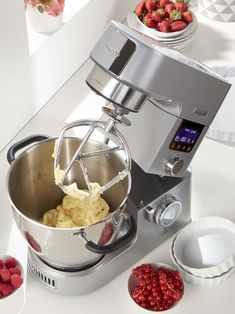 a mixer with some food in it on a white counter next to bowls and plates