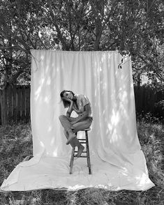 a black and white photo of a woman sitting on a stool in front of a backdrop