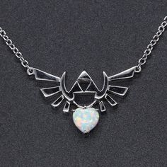 "Can be made in the stone color of your choice at no a additional charge This beautiful necklace is made of pure 925 Sterling Silver and was created as an accent piece to my Legend of Zelda Triforce engagement ring. Though equally as stunning as a stand alone piece. The Hyrule crest is displayed with a heart container suspended from the bottom. Shown in simulated Opal but can be made in any stolen of your choice, Sure to be a cherished heirloom piece. Makes the perfect gift for your special some 8 Bit Heart, Heart Container, Legend Of Zelda Triforce, Zelda Wedding, Heart Video, Geeky Jewellery, Zelda Triforce, Fandom Jewelry, Game Cosplay