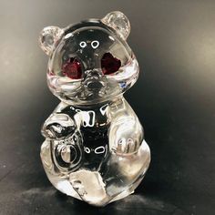 a glass bear figurine with two red eyes on it's face, sitting on a black surface