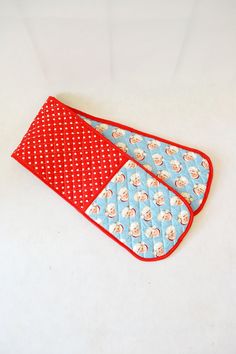 two oven mitts with red and blue designs are on a white surface, next to each other