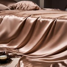 an unmade bed covered in satin sheets and pillows with a candle next to it