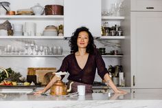 a woman standing in front of a kitchen counter with a tea pot on top of it