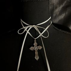 This necklace has a long white ribbon and a metal cross pendant, intended to be wrapped multiple times around the neck. It is about 62 inches long. Adjustable White Cross Necklace, Adjustable White Cross Necklaces, Adjustable Silver Cross Lariat Necklace, White Spiritual Crucifix Cross Necklace, White Crucifix Cross Necklace, Elegant Silver Cross Choker, Adjustable Silver Cross Choker, Elegant Cross Choker As A Gift, Vintage White Cross Jewelry