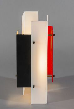 a red and black lamp sitting on top of a white table next to a wall