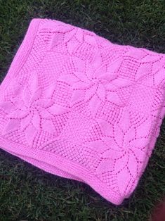 a pink knitted blanket laying on the grass