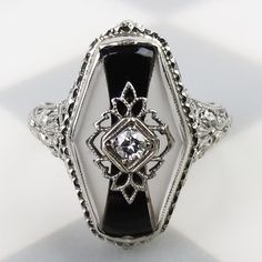 A wonderful elaborate 18k white gold filigree design wraps around the quartz crystal and black onyx stones on this vintage 1930s Art Deco ring. A black onyx bowtie shape flows down the center of the ring. Diamond-shaped matte quartz crystals flank the onyx. A white gold filigree and square shaped setting hold a 2mm diamond above them. The setting is of solid 18k white gold with beautiful floral geometric lattice and millgrain details decorating the gallery. Carved details flow down the shoulders Elegant Gemstone Rings For Evening, Oval White Gold Jewelry With Black Enamel, Classic White Gold Jewelry For Evening, Victorian Black Enamel Rings For Anniversary, Victorian Black Enamel Anniversary Rings, Victorian Black Enamel Wedding Rings, Elegant Oval Evening Rings, Classic White Gold Jewelry With Black Enamel, Formal Black Enamel Fine Jewelry Rings