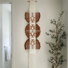 a wall hanging made out of wood and white yarn in a room with a potted plant next to it