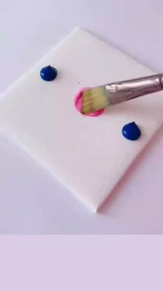 a paintbrush sitting on top of a piece of white paper with blue and pink dots