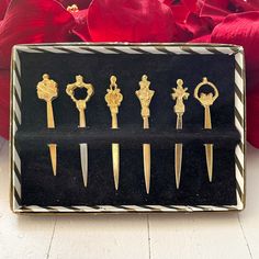 six pairs of gold - plated scissors in a black box next to red flowers