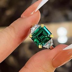 a woman's hand holding a ring with an emerald and white diamond in it