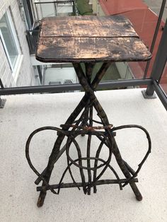 an old wooden table sitting on top of a metal stand next to a glass window