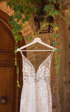 a wedding dress hanging on a hanger in front of an open door with greenery