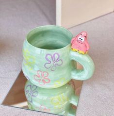 there is a green cup with a pink toy in it on the table next to a mirror