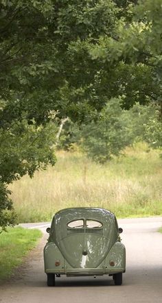 an old green car parked on the side of a road next to trees and grass