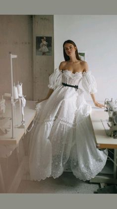 a woman in a white dress standing next to a sewing machine