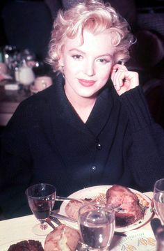 a woman sitting at a table with food in front of her and wine glasses on the side