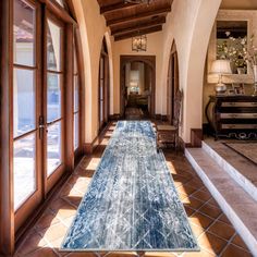 a hallway with an area rug on the floor next to large windows and a chandelier