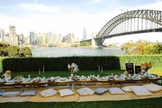 a table set up with plates and silverware in front of the sydney bridge