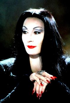 a woman with long black hair and red lipstick posing for a photo in front of a dark background