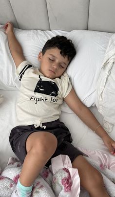 a young boy sleeping on top of a bed with white sheets and pillows in front of him