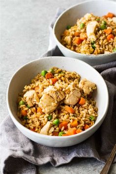 two bowls filled with chicken and rice on top of a table next to a fork