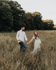 a pregnant couple holding hands and walking through tall grass