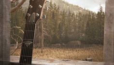 an acoustic guitar sitting on top of a window sill in front of a forest