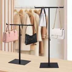 three purses are hanging on the rack in front of a clothing rack with handbags