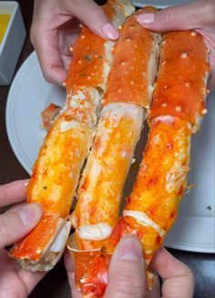 two hands are holding crab legs on a plate