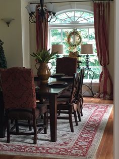 a dinning room table and chairs in front of a window with red drapes